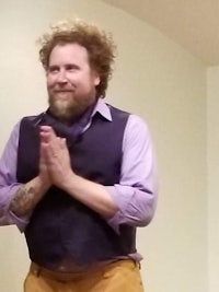 a man with a beard and vest standing in front of a room