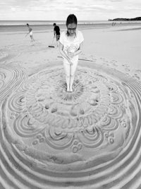 a woman standing on a beach with a sand sculpture