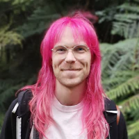 a man with pink hair standing in a forest