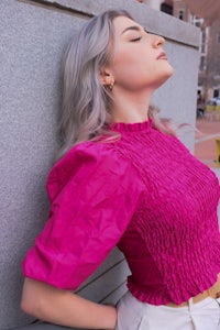 a woman in a pink top leaning against a wall