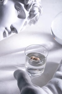 a hand holding a glass of water next to a statue