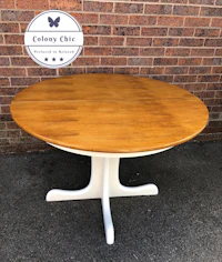 a round wooden table with a white base in front of a brick wall