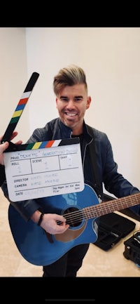a man holding a blue clapboard and an acoustic guitar
