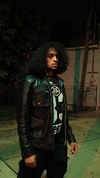 a man in a leather jacket standing on a sidewalk