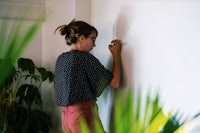 a woman writing on a wall with plants in the background