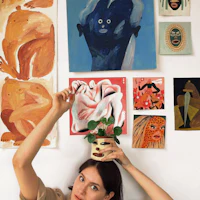 a woman holding a potted plant in front of a wall full of paintings