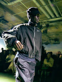 a man walking down a runway in a black jacket and pants