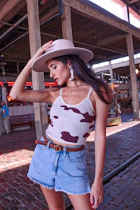 a woman wearing a cow print top and denim shorts