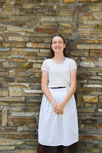 a girl in a white apron standing in front of a stone wall