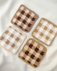 three crocheted checkered coasters on a white surface