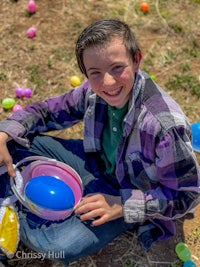 a young boy sitting on the ground with a bucket of easter eggs