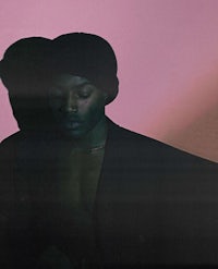 a man in a black jacket is standing in front of a pink wall