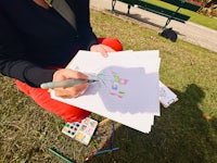 a woman is drawing on paper in a park