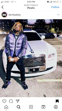 a man with dreadlocks standing next to a white car