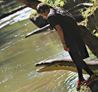 a man standing on a log next to a river with a snake