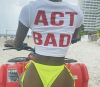 a woman in a bikini on a beach wearing a t - shirt that says act bad