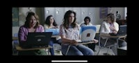a group of girls sitting in a classroom with laptops