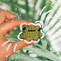 a person holding a green crocheted frog