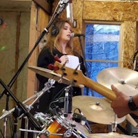 a woman singing and playing drums in a recording studio