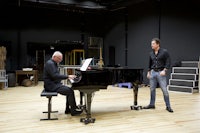 two men standing next to a piano in a room