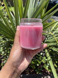 a hand holding a pink candle in front of a palm tree