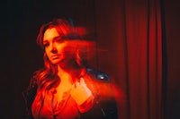 a woman in a leather jacket standing in front of a red curtain