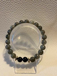 a black and gold beaded bracelet on a clear surface