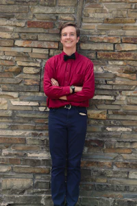 a man in a red shirt and blue pants standing against a brick wall
