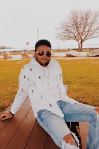 a man sitting on a bench with sunglasses and ripped jeans