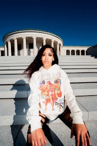 a woman wearing a sweatshirt sitting on steps in front of a building