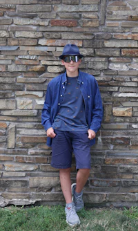 a young man leaning against a stone wall wearing a hat and shorts