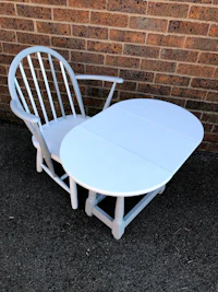 a white rocking chair with a white table in front of a brick wall