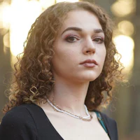 a young woman with curly hair standing in the woods