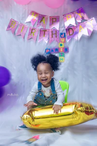 a baby sitting on a gold balloon in front of balloons