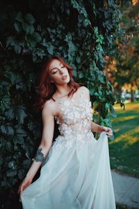 a red haired woman in a white dress leaning against a tree