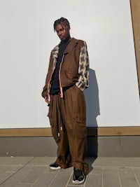 a man in a brown jacket posing in front of a wall
