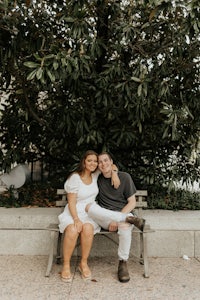 a couple sitting on a bench in front of a tree