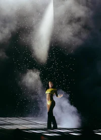 a woman is standing on a stage with smoke coming out of it