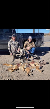 two men posing next to a truck full of dead animals