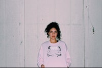 a woman in a pink sweatshirt posing against a wall