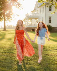 two girls holding hands in front of a large house