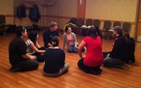 a group of people sitting in a circle on a wooden floor