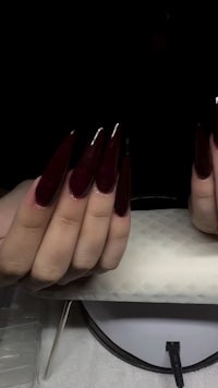 a woman's hands with long burgundy nails on a table