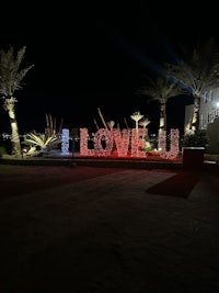 a sign lit up at night with palm trees in the background