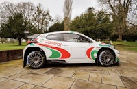 a green and white rally car parked in front of a tree