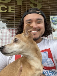 A man with a hat on holding a chihuahua 