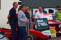 a group of men standing next to a red car