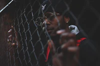 a man wearing glasses and a backpack looking through a chain link fence