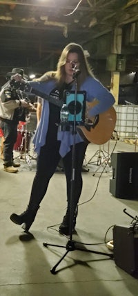 a woman singing and playing an acoustic guitar in a warehouse