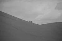 two people standing on top of a sand dune